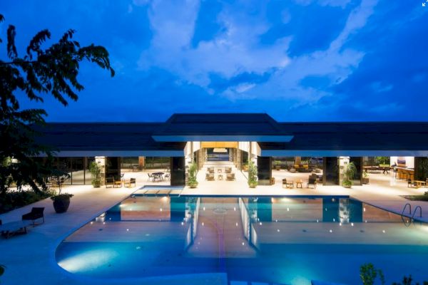 A luxurious building with an illuminated pool in the foreground under a twilight sky, surrounded by outdoor seating.