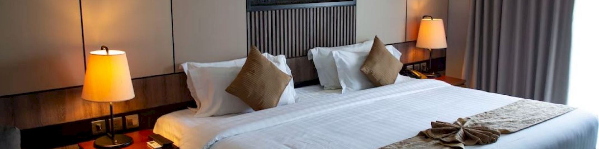 A neatly arranged hotel room features a large bed, decorative pillows, and soft lighting, creating a cozy and inviting atmosphere.