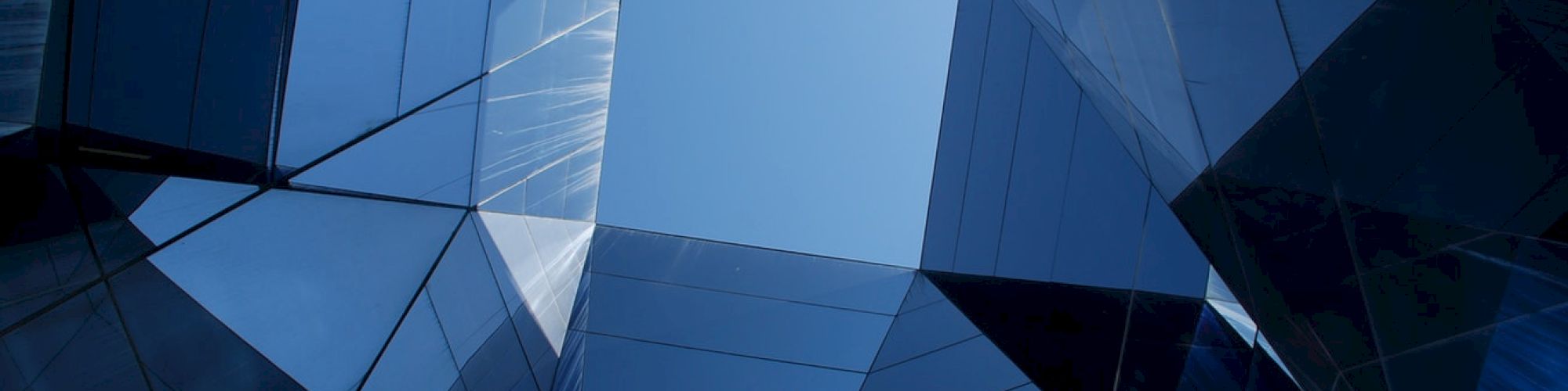 Geometric architecture with reflective surfaces creates an abstract, mirrored view looking up at the sky through a symmetrical opening.