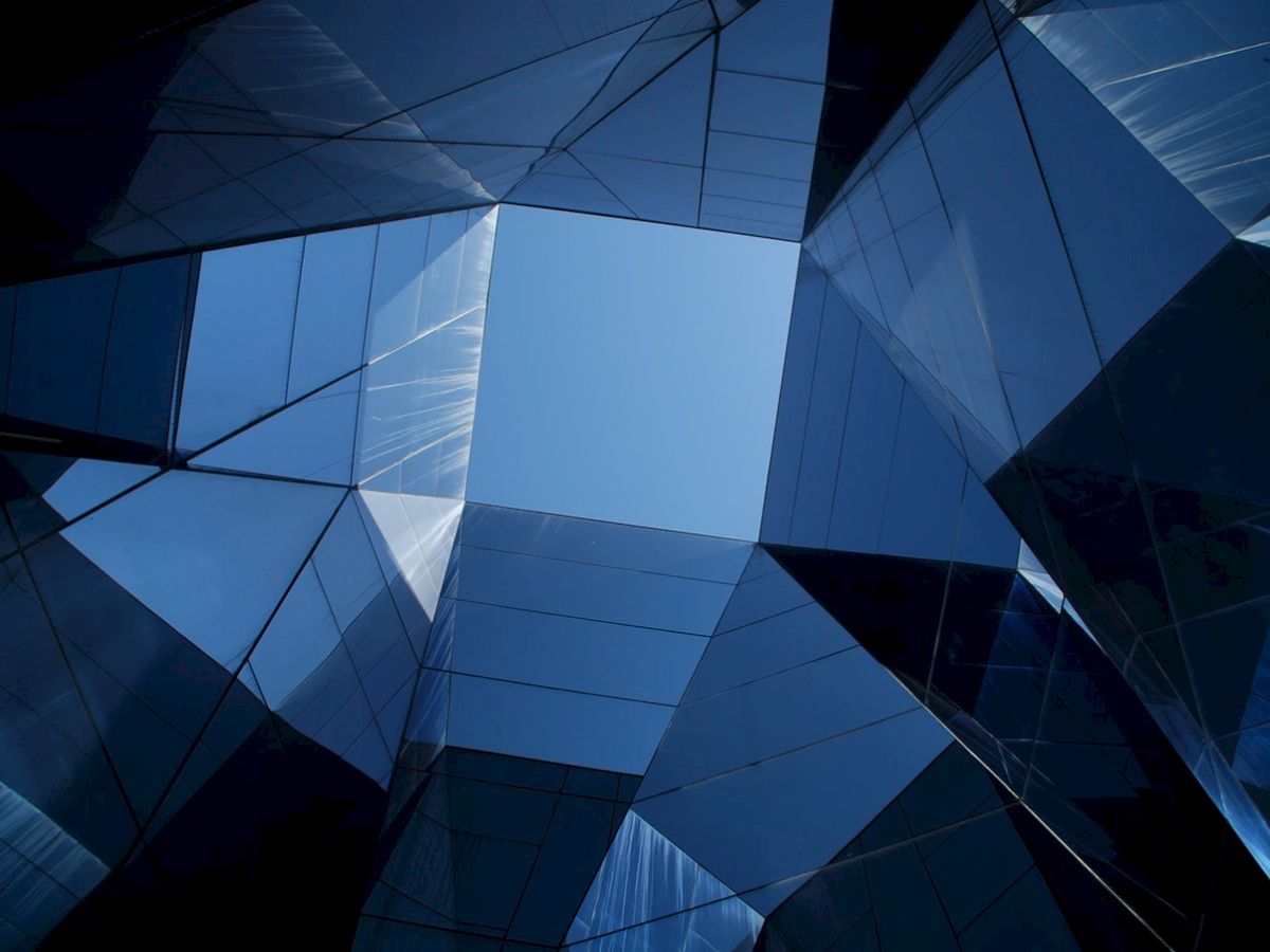 Modern glass buildings form a geometric pattern against the blue sky, creating a striking architectural view from below.