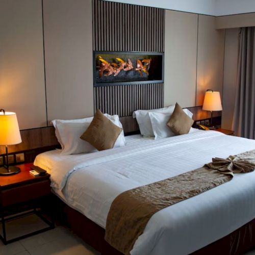 A cozy hotel room with a large bed, two bedside lamps, decorative pillows, and a small fireplace above the bedhead.