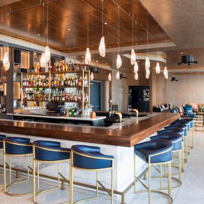 A modern bar with a central counter, stylish chairs, hanging lights, and a well-stocked back bar in an open, elegantly designed space.