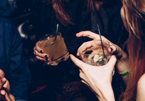 People are socializing and holding drinks in a lively setting, with laughter and animated gestures.