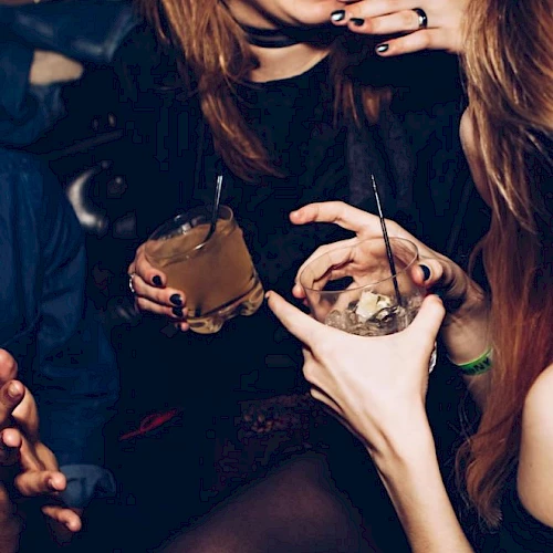 People are socializing and holding drinks in a lively setting, with laughter and animated gestures.