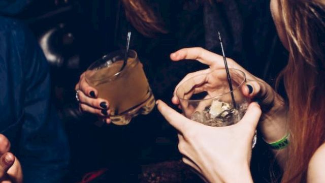 People are socializing and holding drinks in a lively setting, with laughter and animated gestures.