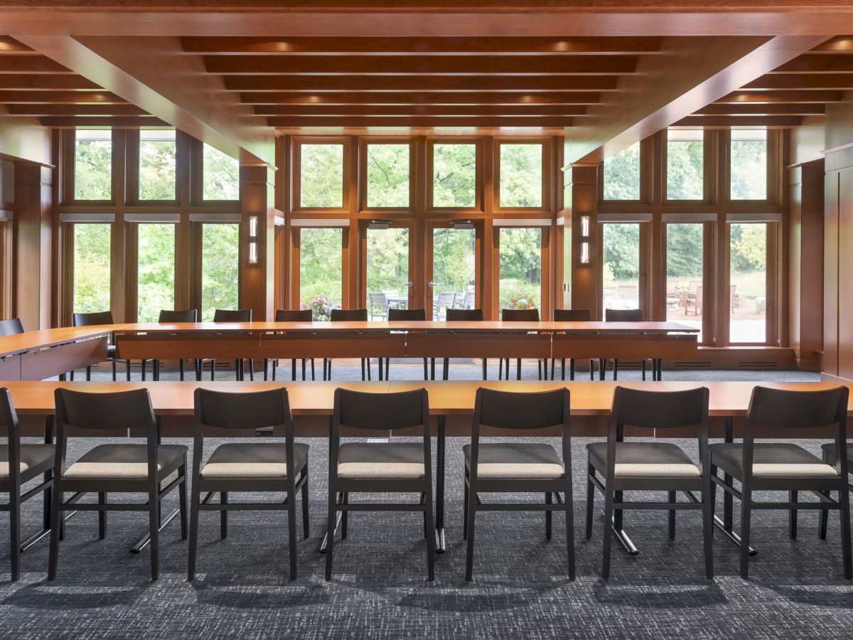 A conference room with wooden paneling, large windows, and rows of chairs arranged around a long table, ready for a meeting.