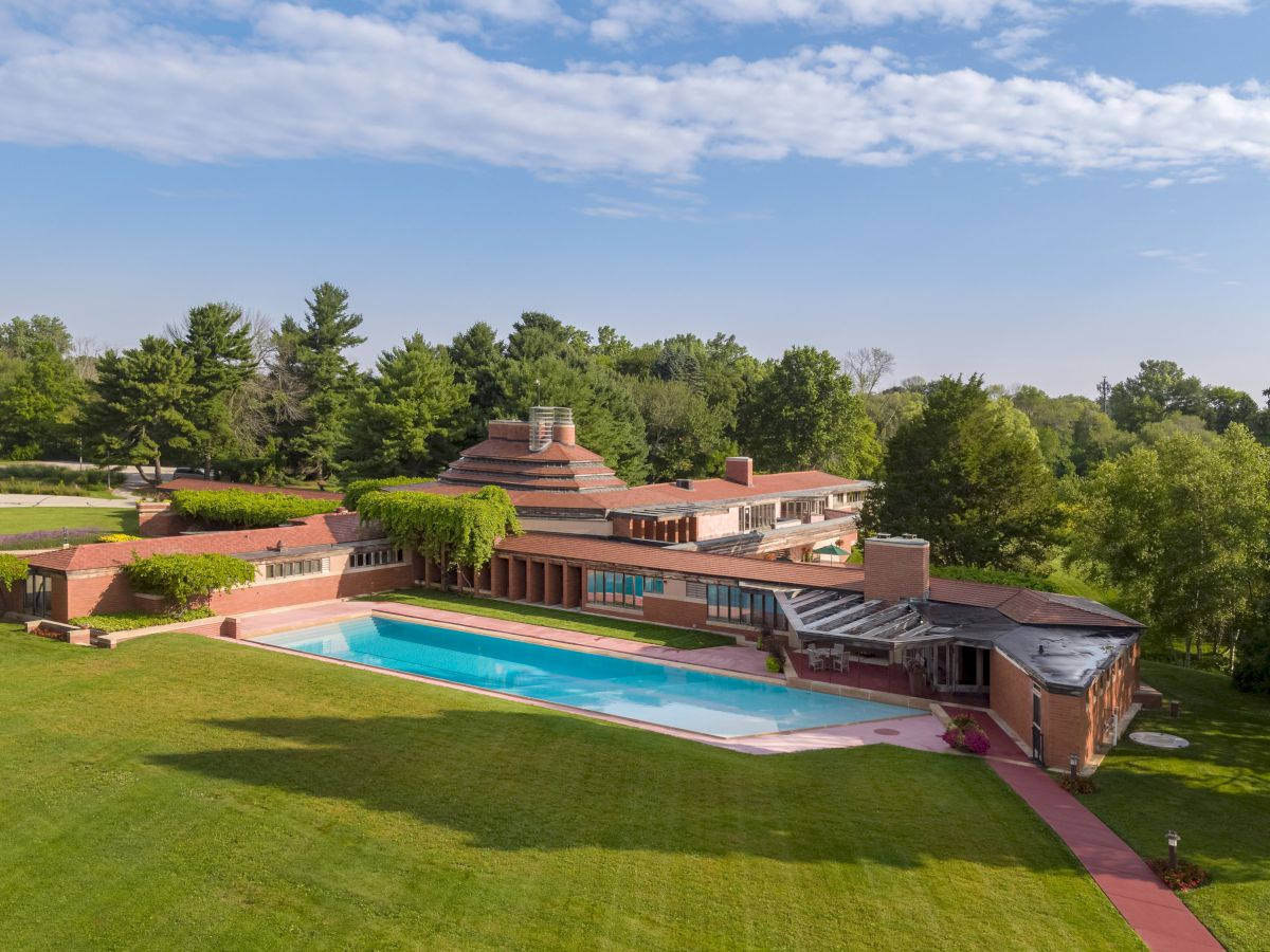 A spacious property features a large modern house with a unique design, surrounded by a well-kept lawn and a swimming pool.