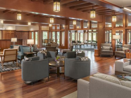 The image shows a spacious, elegant lobby with wooden floors, cozy seating arrangements, and large windows. Warm lighting enhances the ambiance.