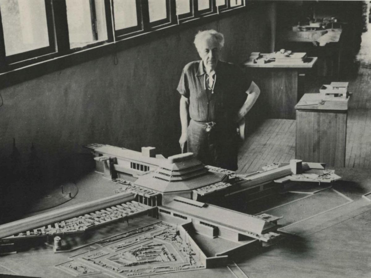 A person stands next to a large architectural model displayed indoors, with additional models visible in the room.