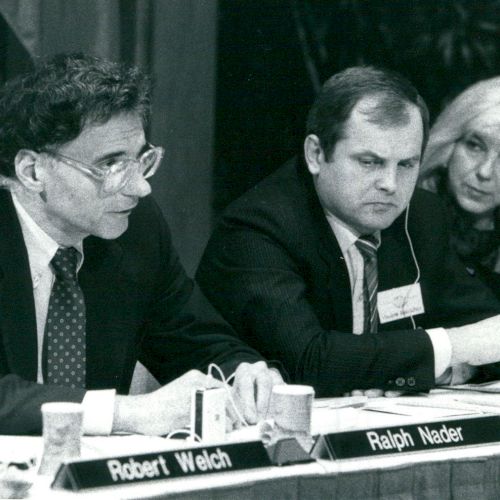 A group of three people seated at a table with nameplates, engaged in a discussion.