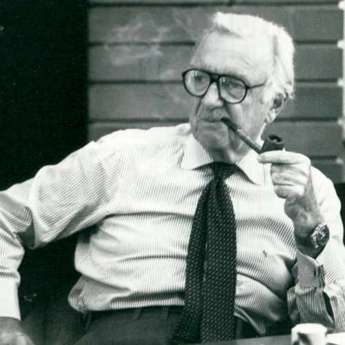 A person is sitting and smoking a pipe, wearing glasses, a striped shirt, and a tie, with smoke visible in the air around them.