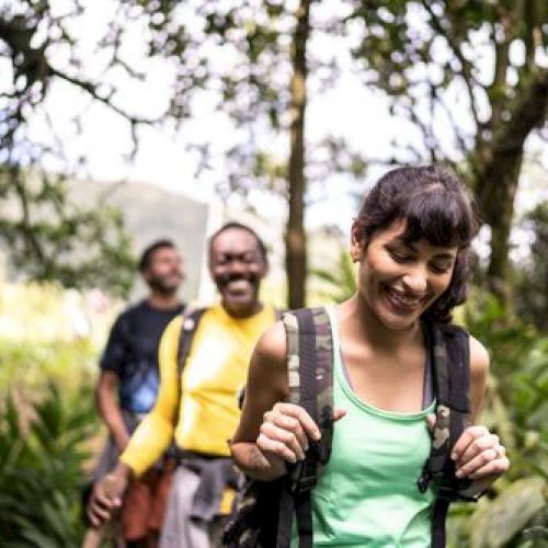 Three people are hiking through a lush forest, smiling and enjoying the outdoors.