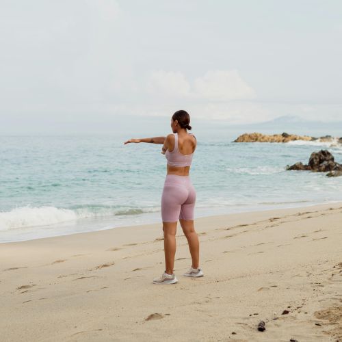 A person standing on a sandy beach, facing the ocean, wearing athletic attire, with arms outstretched and waves in the background.