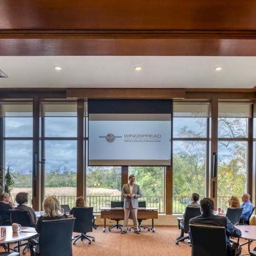 A bright modern kitchen or dining area with large windows, people chatting at a table, and warm wooden accents, creating a cozy social scene.