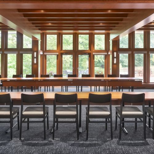 The image shows a conference room with wooden decor, large windows, and arranged chairs around tables, creating an organized and inviting space.