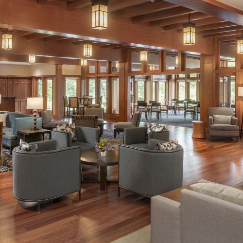 The image shows a spacious, elegantly furnished lobby with wooden accents, cozy seating, and warm lighting, creating a welcoming ambiance.