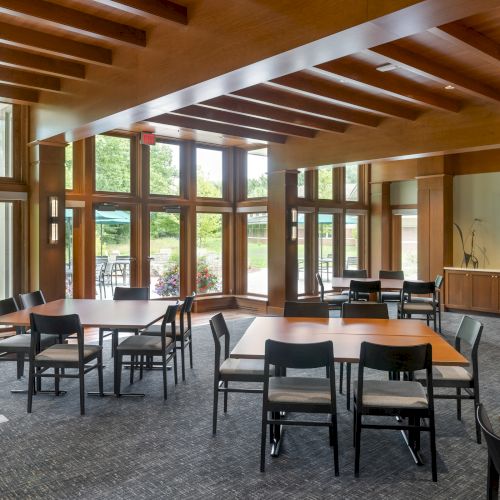 The image shows a modern conference room with wooden tables and chairs, large windows, and a screen displaying "The Village Club.".