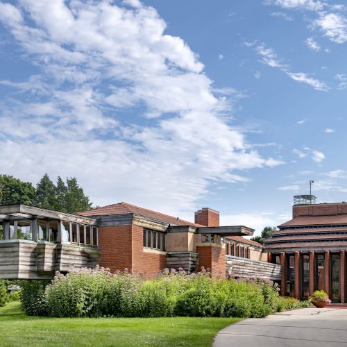 A modern architectural building with brick, glass, and greenery under a partly cloudy sky.