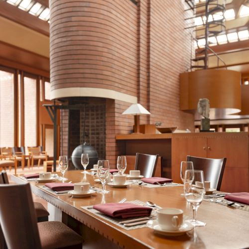 A spacious dining room with a large table set with glasses, plates, and napkins, and surrounded by modern architecture and natural light.