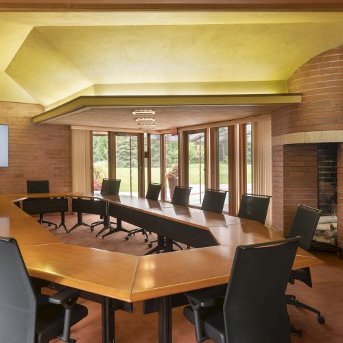 The image shows a modern conference room with a large U-shaped table, black chairs, a fireplace, and a screen displaying "Johnson Foundation."