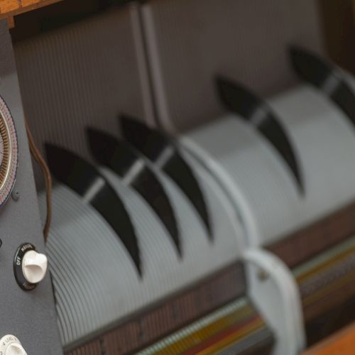 The image shows a close-up of a vintage music player mechanism with dials, knobs, and a rotating drum with perforated patterns.