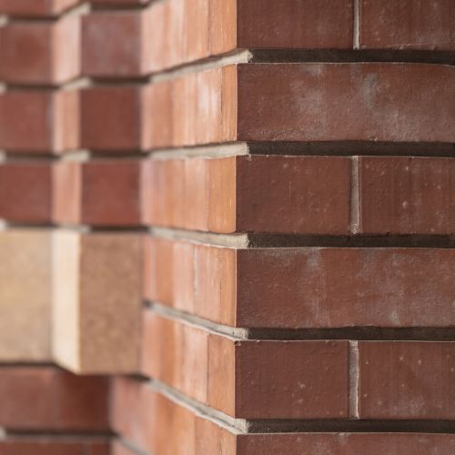 A close-up of a brick wall corner showing red bricks and mortar with a beam extending horizontally, possibly part of a building structure.
