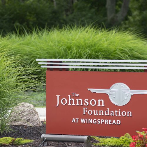 The image shows a sign for "The Johnson Foundation at Wingspread" set against greenery and landscaping.