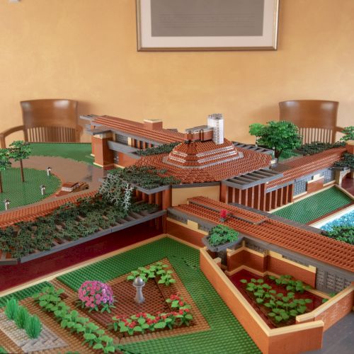 A detailed LEGO model of a large building with green landscaping, trees, and a pool on a table.