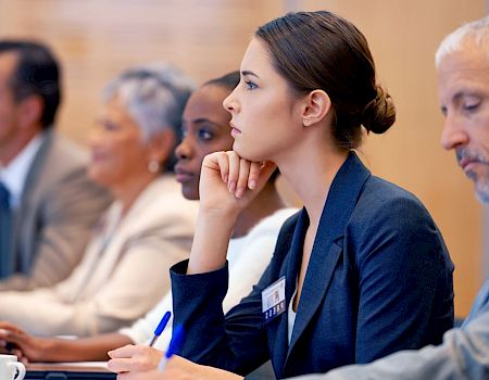 A diverse group of people in professional attire are seated at a conference or meeting, engaging attentively in a discussion.