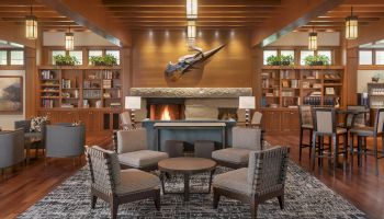 A cozy lounge with a fireplace, seating area, bookshelves, and decor under wooden beams, creating a warm and inviting atmosphere.
