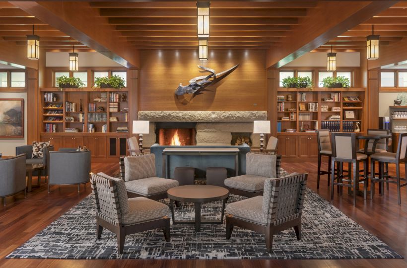 A cozy lounge with a fireplace, seating area, bookshelves, and decor under wooden beams, creating a warm and inviting atmosphere.