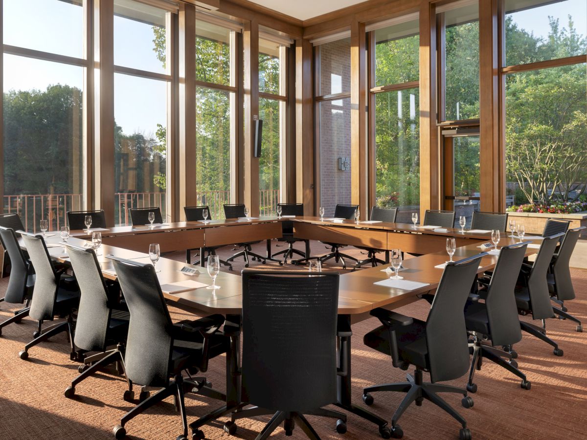 A modern conference room with a U-shaped table setup, surrounded by office chairs and large windows providing a scenic outside view.