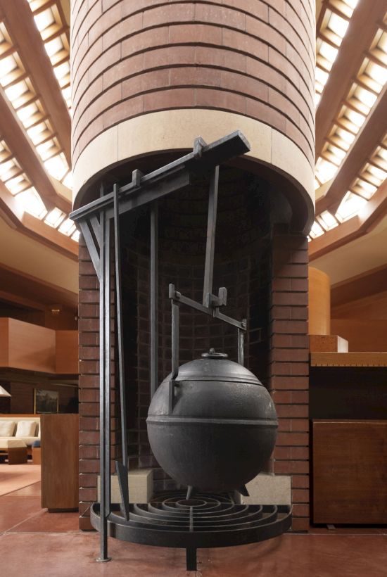 The image shows a unique, circular fireplace with a hanging cauldron-like structure in a room with wooden and brick architecture.