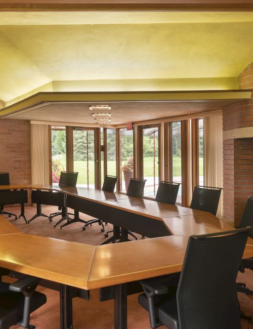 A conference room with a large, uniquely shaped table, black chairs, a fireplace, and a screen displaying "Johnson Foundation."