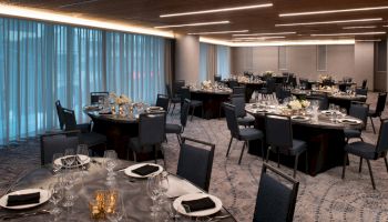 The image shows an elegantly set dining room with round tables, chairs, and ambient lighting, ready for an event or banquet.