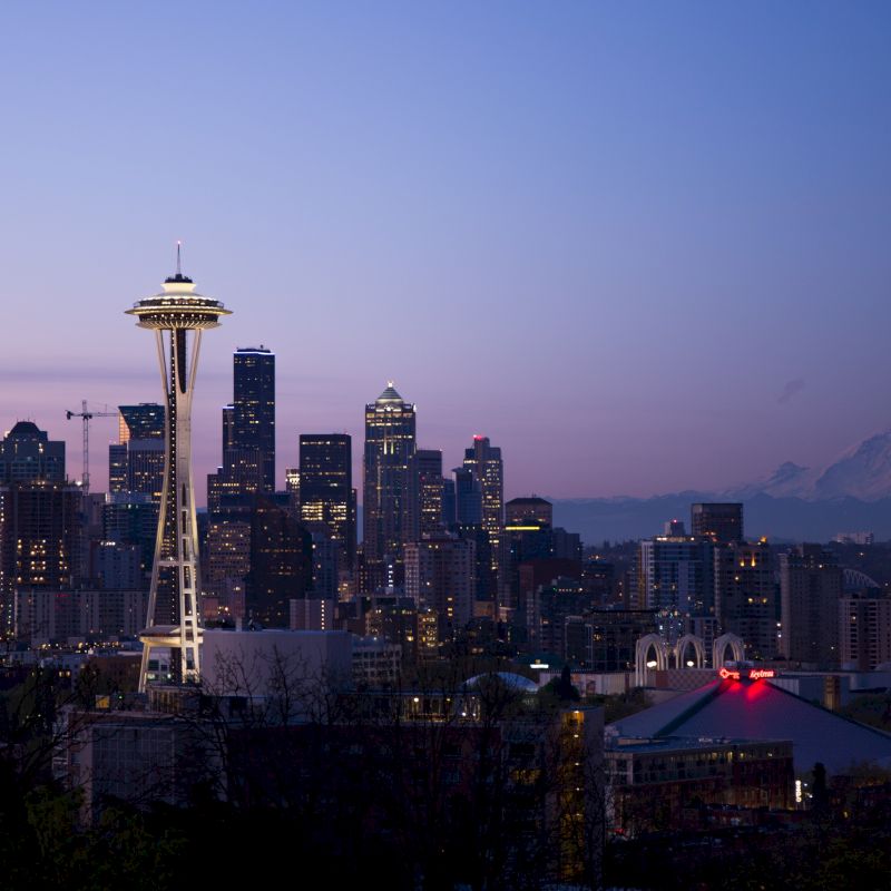 The image shows a twilight view of Seattle's skyline, with the Space Needle and Mount Rainier in the background.