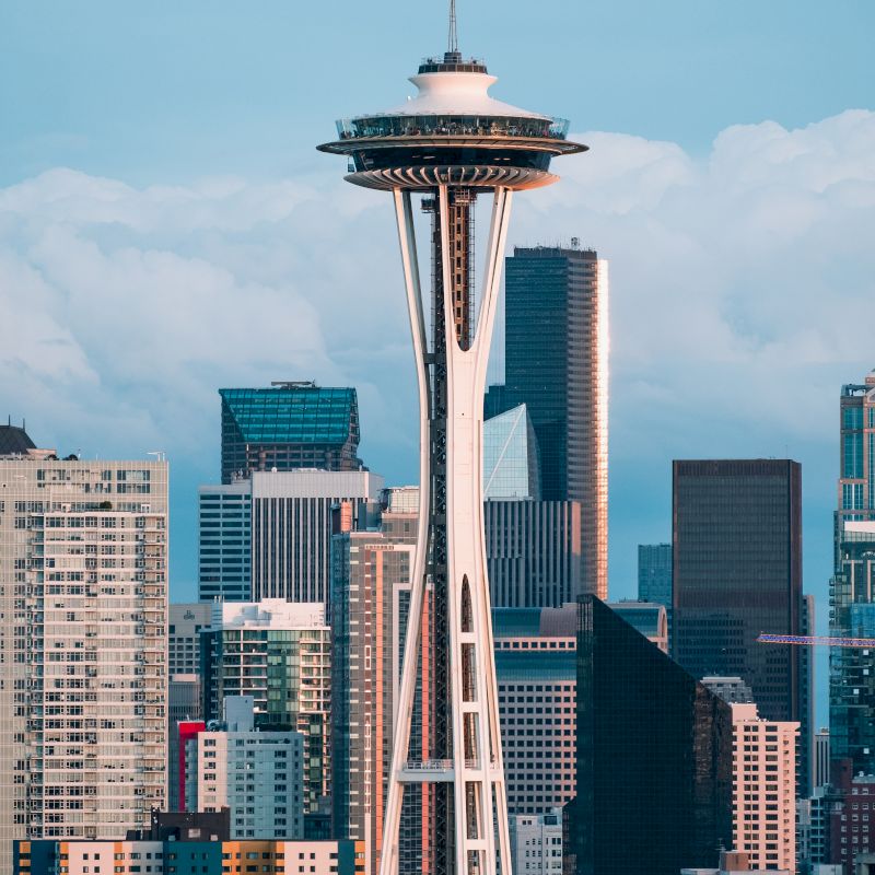 The image shows a city skyline featuring a prominent observation tower and various skyscrapers against a backdrop of cloudy skies.
