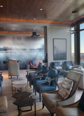 A modern lounge with seating, a mural of a city skyline on the wall, and large windows offering a view of the ocean and a Ferris wheel.