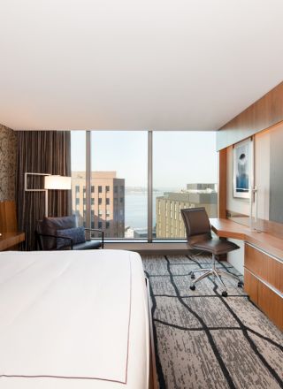 A modern hotel room with a large bed, desk, chair, flat-screen TV, and a window with a city view completes the contemporary ambience.